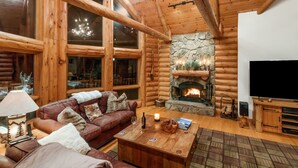 A log cabin interior with a stone fireplace, leather sofa, and a television.