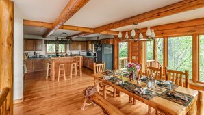 A wooden interior with a dining table set for four, wooden beams on the ceiling, and large windows.