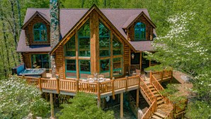 A log cabin with a large deck, hot tub, and multiple windows.