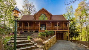 A log cabin with a porch, stone steps, and a view of the surrounding forest.