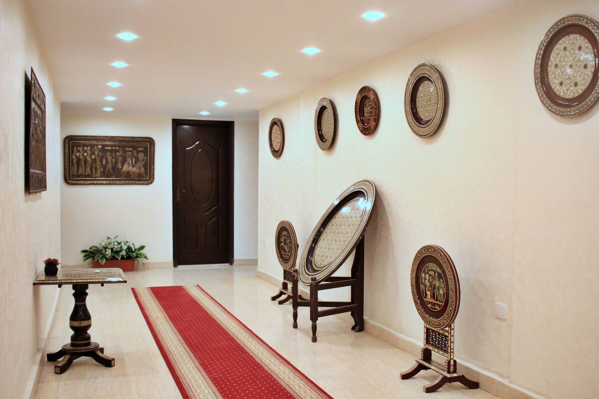 A hallway with a red carpet, a table with a vase, and several wall-mounted mirrors.