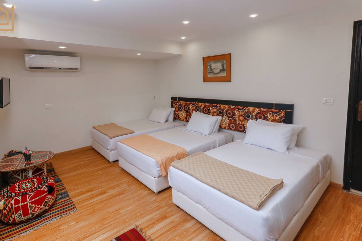 A hotel room with two beds, a wooden floor, an air conditioner, a television, and a door.