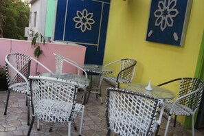 Un patio con sillas y mesas de mimbre, un muro rosa y detalles decorativos en la pared.