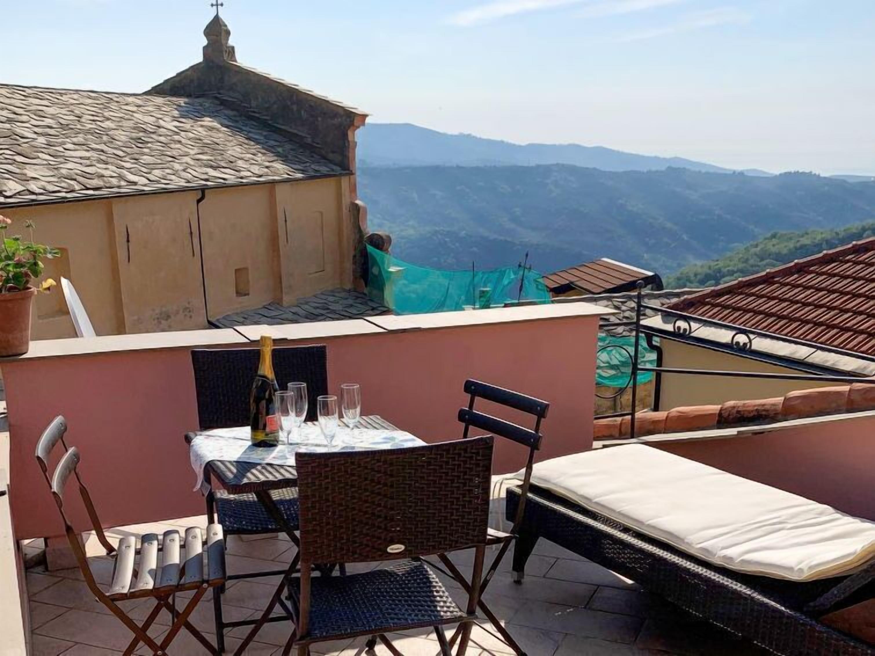 A rooftop terrace with a table set for two, a chair, and a mattress.