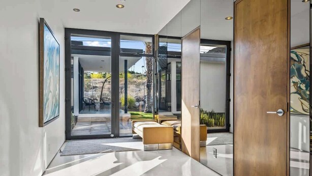 Un interior moderno con un vidrio que da a un espacio exterior, una puerta de madera y un cuadro en la pared.