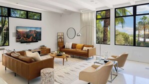 Una sala de estar moderna con un sofá, una mesa de centro y sillas, ventanas amplias con vistas, y un cuadro en la pared.