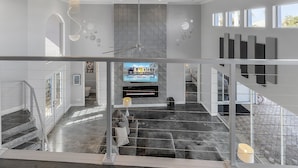 Een ruim interieur met een trap, een kroonluchter en een wandtelevisie waarop een logo wordt getoond.