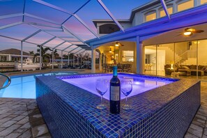 A swimming pool with a glass enclosure, a bottle of wine, and two wine glasses on the edge. - Custom Pool with a NEW hot tub, Bikes, and Gulf Access! - Villa Whispering Palms - Roelens Vacations (Cape Coral)