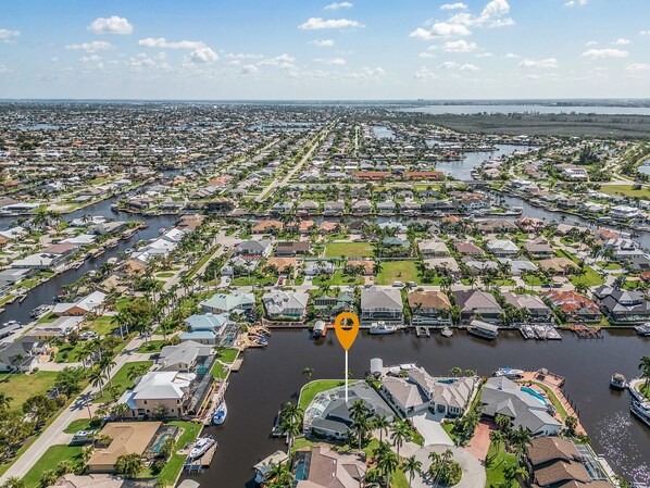 An aerial view of a residential area with a marina, featuring houses, boats, and a clear sky. - Custom Pool with a NEW hot tub, Bikes, and Gulf Access! - Villa Whispering Palms - Roelens Vacations (Cape Coral)