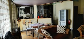Un espacio habitable compacto con zona de comedor, kitchenette y sofá con cojines estampados.