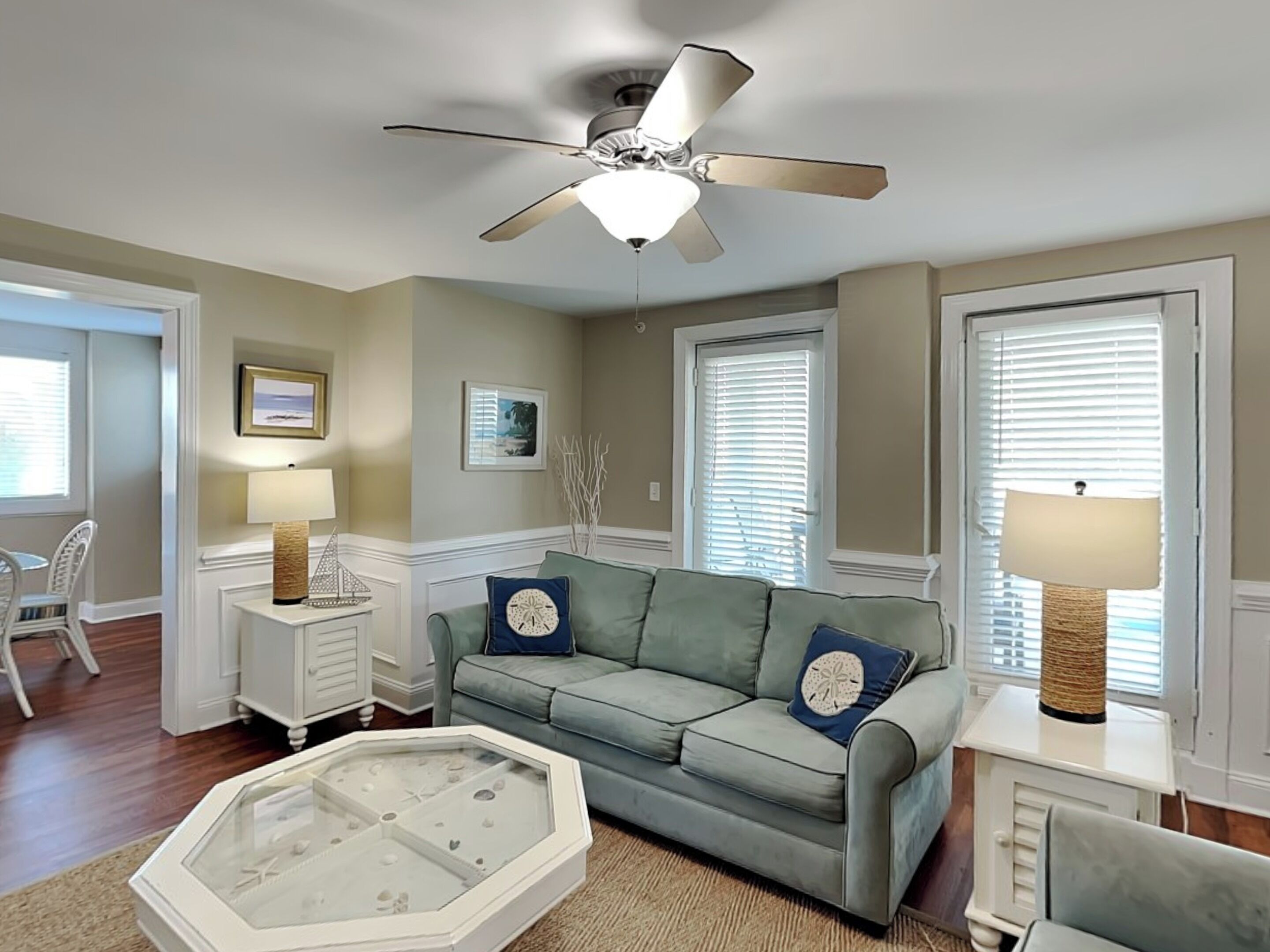 A living room with a light green sofa, two clocks, a ceiling fan, and a glass-top coffee table.