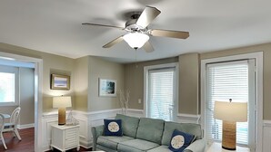 A living room with a light green sofa, two clocks, a ceiling fan, and a glass-top coffee table.