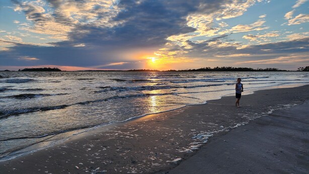 A beach scene with a person walking along the shore during sunset.
