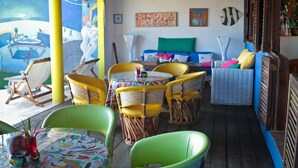 Un espace extérieur aménagé, abrité et doté de chaises et d’une table en osier, d’un canapé bleu et d’une fresque murale.