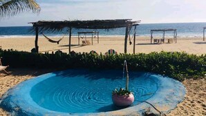 Une plage avec une petite piscine, une structure à toit de chaume et une vue sur l’océan.