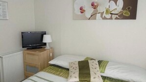 A bedroom with a bed, a television on a wooden nightstand, and a wall-mounted picture of flowers. - Tiny Single shared bathroom Room ssbyr (Hayes)
