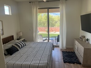 A bedroom with a bed, a nightstand, a TV, a dresser, and a view of a patio with a table and chairs.