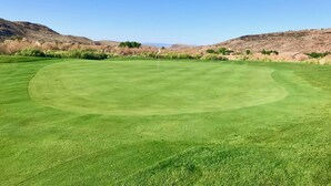Een goed onderhouden golfbaan met een herkenbare vlag, omgeven door droog gras en heuvels.