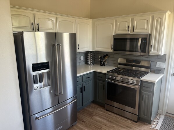A modern kitchen with stainless steel appliances, white cabinets, and a grey tiled backsplash.