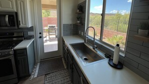 Een moderne keuken met een ingebouwde magnetron, kookplaat en spoelbak. Er is een raam met uitzicht op het omliggende landschap.