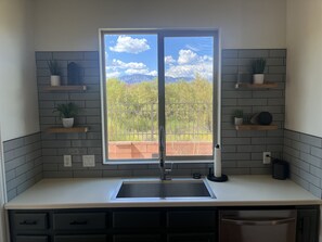 A kitchen with a large window, a sink, and two shelves with plants. - 30+ Day Stays - Quiet, Pet-Friendly, Pool & Views (Washington)
