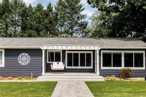 Een huis met twee verdiepingen, een veranda, een kompasbord en een kleine tuin.