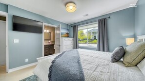 A bedroom with a bed, a TV, a dresser, and a window with a view.