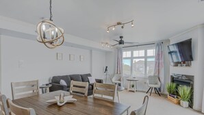 Moderni olohuone, jossa on puinen ruokapöytä, harmaa sohva, kattotuuletin, seinälle asennettu televisio ja takka.