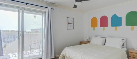 Une chambre avec un lit, un ventilateur de plafond, une fenêtre donnant sur des immeubles et un mur décoré avec des motifs de sucettes glacées.