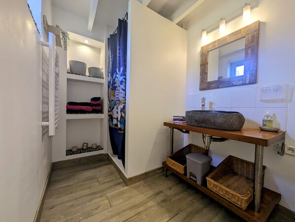 A bathroom with a wooden vanity, a large mirror, and a shelf with folded towels. - Mas en Provence Avec SPA Privé (Carpentras)