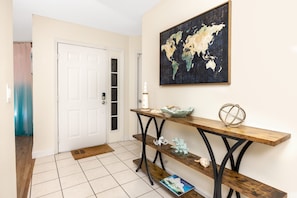 A hallway with a white door, a world map on the wall, a wooden console table with decorative items, and a tiled floor. - Endless summer in beautiful house with heated pool (Bradenton)