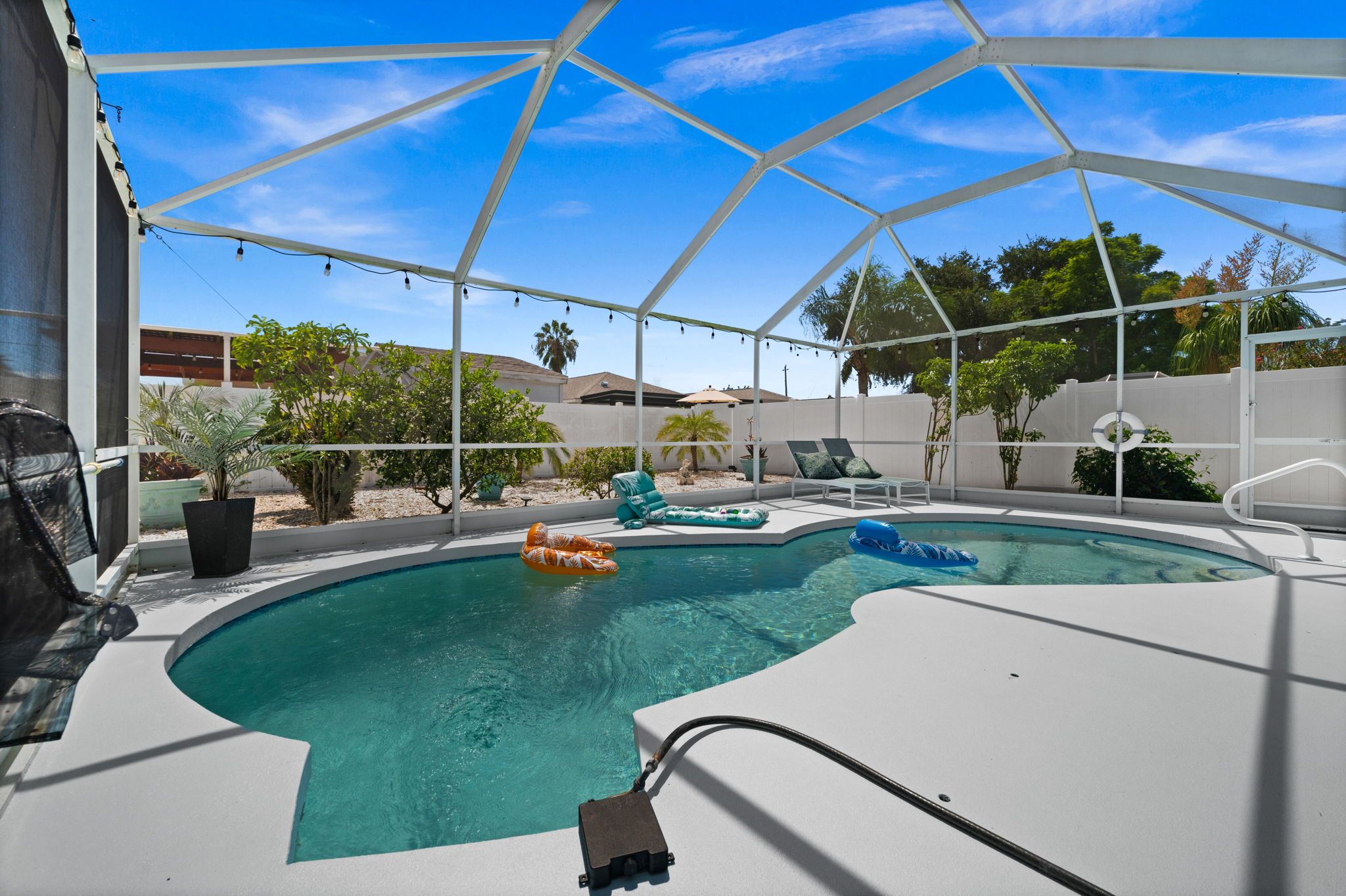 A swimming pool with a white deck, surrounded by a covered area with lounge chairs and umbrellas.