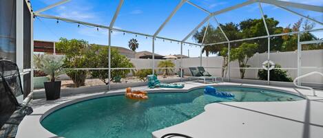 A swimming pool with a white deck, surrounded by a covered area with lounge chairs and umbrellas.