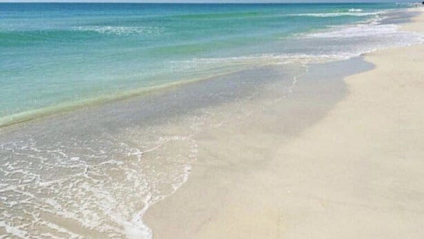 Une plage avec une eau d’un bleu limpide et un rivage sablonneux.