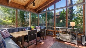 Um quarto iluminado pelo sol, com teto de madeira, janelas amplas, mesa de jantar, cadeiras, sofá e um espaço para vinhos.