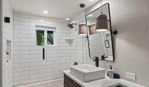 Un baño moderno con azulejos blancos tipo metro, un espejo grande, un lavamanos blanco y una ventana.