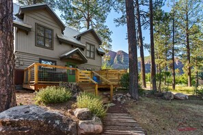 A log cabin with a deck, surrounded by trees and a mountain view.
