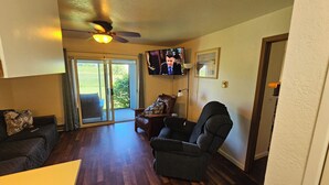 A living room with a ceiling fan, a television mounted on the wall, a large window with a view of the outdoors, and a sliding glass door leading to a patio. - 1ST floor Condo NO STAIRS, beaches ,pool cedar point camp perry marsh parks,<br> (Oak Harbor)