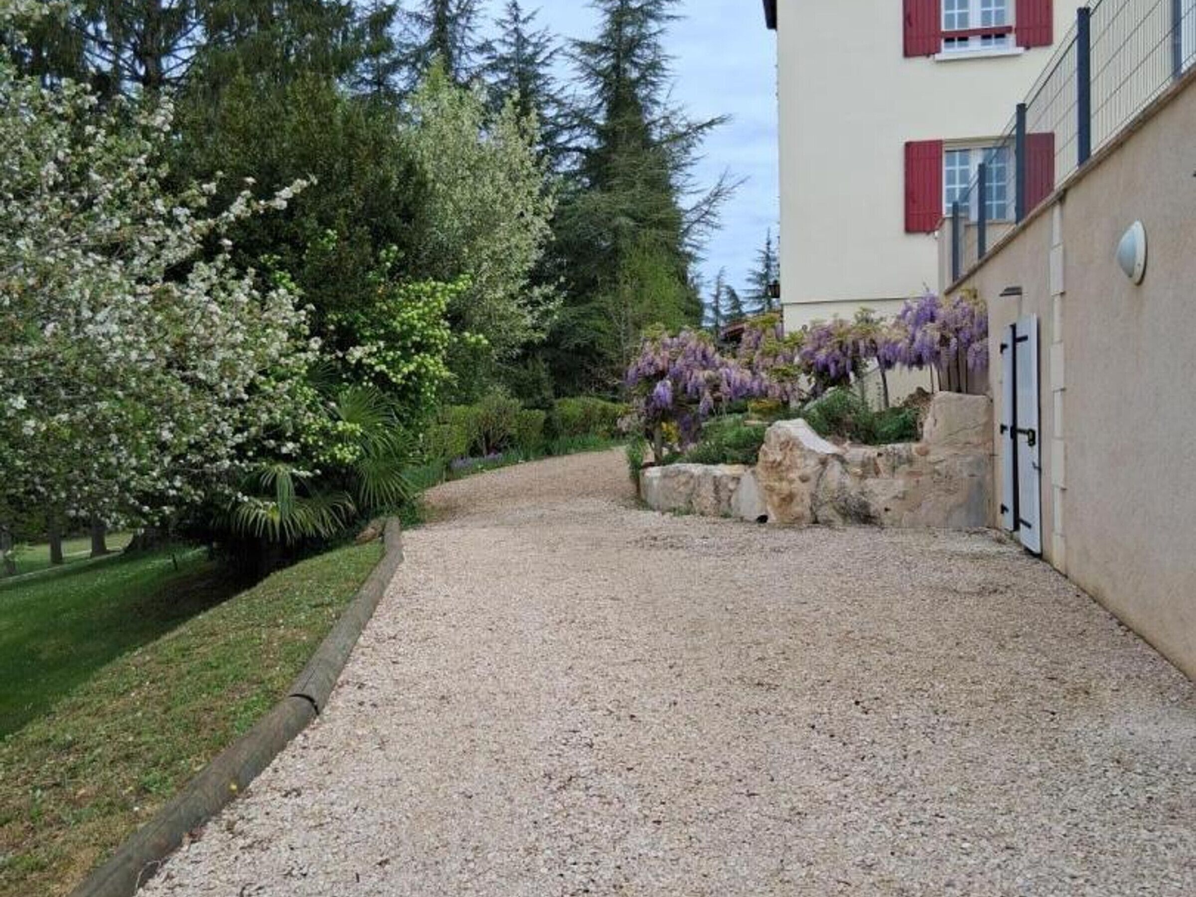 Une allée de gravier mène à un bâtiment doté d’un mur en pierre et d’une porte.
