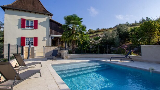 A poolside area with a pool, lounge chairs, and a building with red shutters.