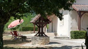 A covered outdoor seating area with a stone table and chairs, a red umbrella, and a building with a tiled roof in the background. - Spacious house with fireplace and large garden in Thiviers (Thiviers)