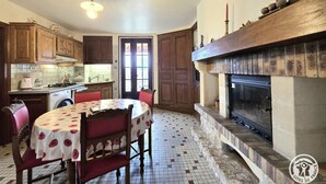 A kitchen with wooden cabinets, a round dining table with a polka dot tablecloth, and a fireplace with a stone surround. - Spacious house with fireplace and large garden in Thiviers (Thiviers)