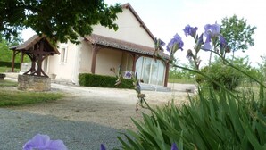 A building with a stone structure in front, surrounded by greenery and purple flowers. - Spacious house with fireplace and large garden in Thiviers (Thiviers)