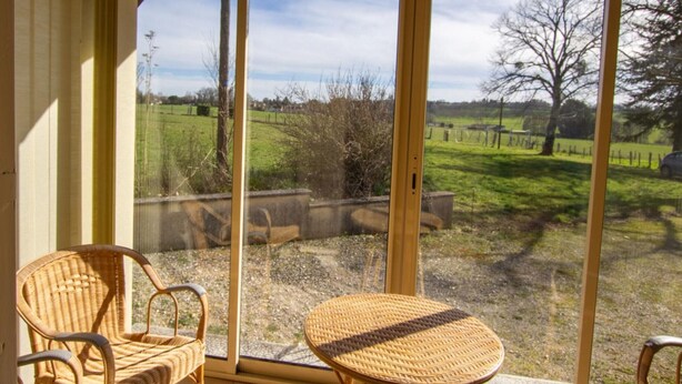 A room with a large sliding glass door leading to a grassy outdoor area. There are two wicker chairs and a small round table in the room. - Spacious house with fireplace and large garden in Thiviers (Thiviers)