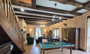 A spacious room with a pool table, wooden beams, a chandelier, and a deer head mounted on the wall.