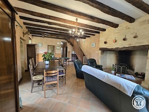Un coin repas rustique avec une table et des chaises en bois, une cheminée et un escalier menant à une autre pièce.