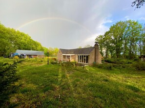 Ein Haus mit einem Steinkamin, einer Glastür und einem Garten mit Gras und Bäumen.