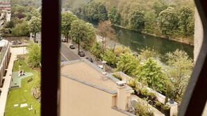 Blick aus einem Fenster auf einen Fluss, einen Park und entfernte Gebäude.