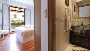 A hotel room with a bed, a chair, a bathroom with a glass sink, and a view of the outside. - Aire de La Concha | The Rentals Collection (San Sebastián)