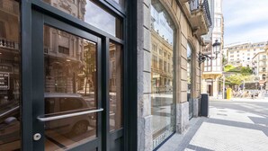 A building entrance with a glass door, a metal handle, and a visible car parked outside. - Aire de La Concha | The Rentals Collection (San Sebastián)